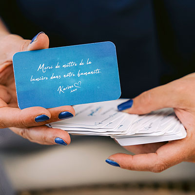 Carte Passez au suivant avec le message 'Merci de mettre de la lumière dans votre humanité' tenue en main, fond bleu.