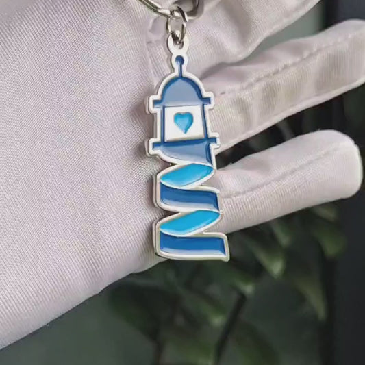 Porte-clé en métal représentant le logo Simplement Humain, tenu par une main gantée blanche. Design moderne et élégant avec des teintes de bleu.