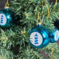 Boule de Noël turquoise avec le logo Simplement Humain dans un sapin.